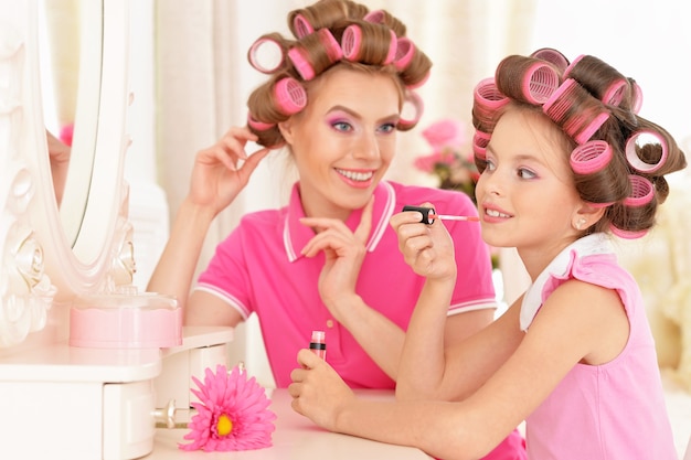 Portrait d'une mère heureuse et d'une petite fille en bigoudis près du miroir