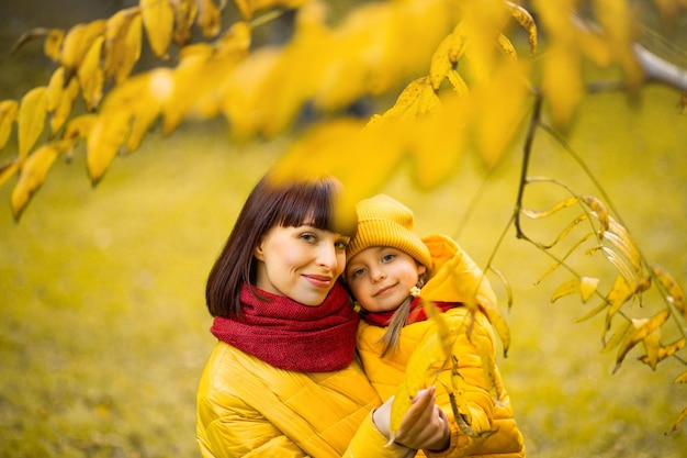 Portrait d'une mère heureuse tenant sa petite fille et posant devant la caméra parmi un bel arbre d'automne doré à l'extérieur dans le parc.