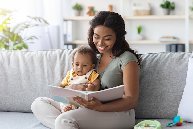 Portrait d'une mère noire attentionnée lisant un livre à un petit bébé à la maison