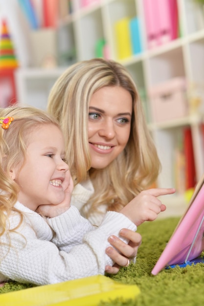 Portrait de mère avec petite fille lisant un livre en position couchée sur le sol