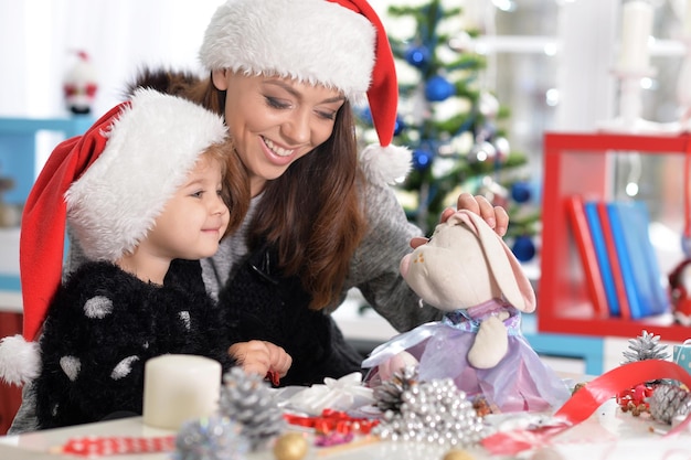 Portrait d'une mère souriante et d'une petite fille mignonne se préparant pour Noël à la maison portant des chapeaux de Père Noël