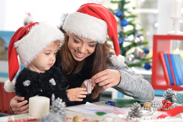 Portrait d'une mère souriante et d'une petite fille mignonne se préparant pour Noël à la maison portant des chapeaux de Père Noël