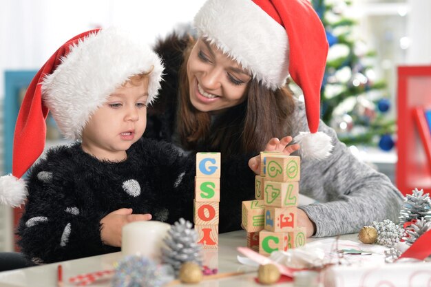 Photo portrait d'une mère souriante et d'une petite fille mignonne se préparant pour noël à la maison portant des chapeaux de père noël