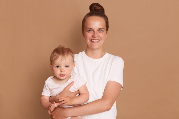 Portrait d'une mère souriante satisfaite tenant une petite fille heureuse famille s'amusant ensemble adorable enfant dans les bras de maman maman et enfant isolés sur fond marron