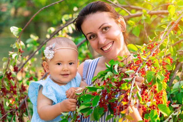 Portrait d'une mère tenant sa fille nouveau-née dans ses bras parmi les branches vertes du cerisier des oiseaux. Baies rouges du cerisier des oiseaux