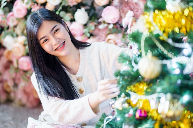 Portrait Mignon beau sourire positif jeune femme asiatique décorant un arbre de Noël à la maison dans le salon à l'intérieur Décoration Pendant les vacances de Noël et du Nouvel An.