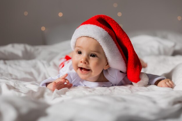 Portrait d'un mignon bébé dans un chapeau de Père Noël souriant dans le lit à la maison le matin de Noël photo de haute qualité