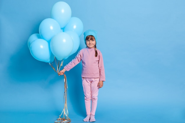 Portrait de mignon enfant d'âge préscolaire posant contre le mur bleu avec des ballons