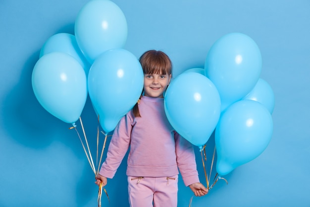 Portrait de mignon enfant d'âge préscolaire posant contre le mur bleu avec des ballons