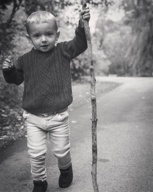 Photo portrait d'un mignon garçon avec un bâton qui marche sur la route