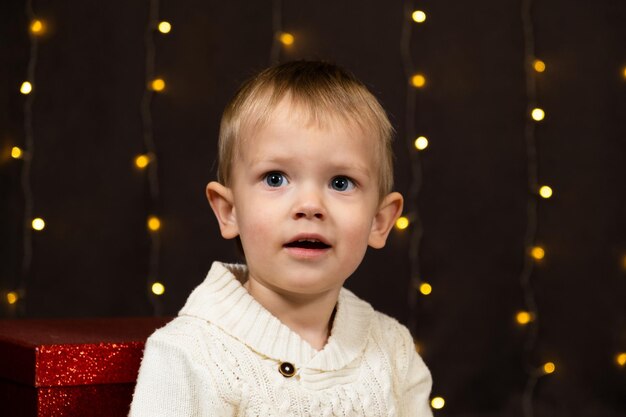 Portrait d'un mignon garçon de deux ans sur le fond d'une guirlande bokeh chez les enfants de Noël