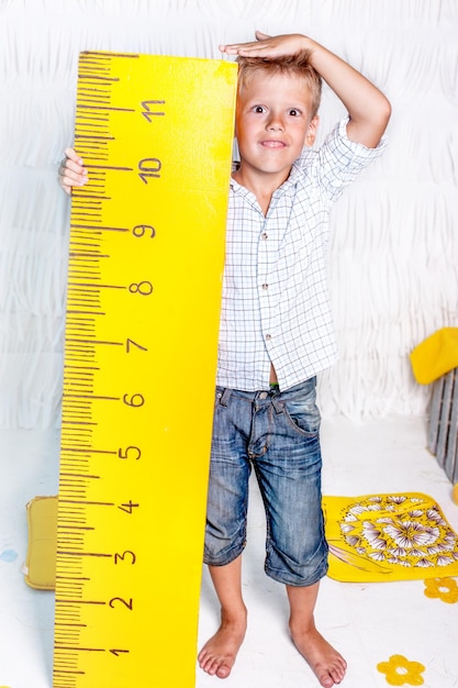 Photo portrait d'un mignon garçon souriant qui mesure sa taille à la maison