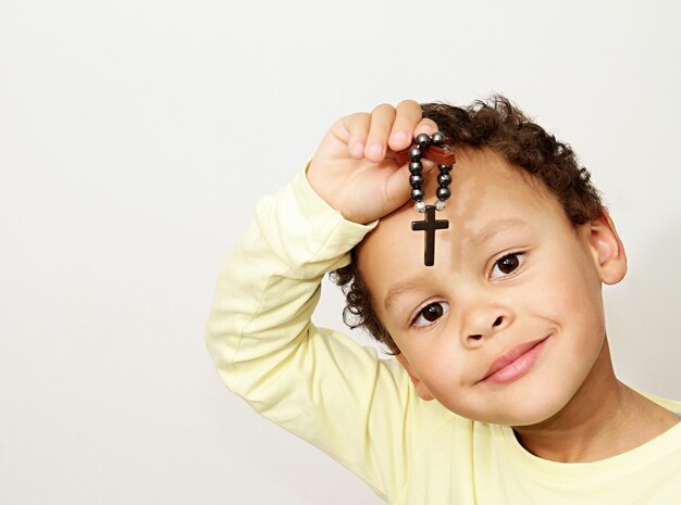 Portrait d'un mignon garçon tenant une croix en prière sur un fond blanc