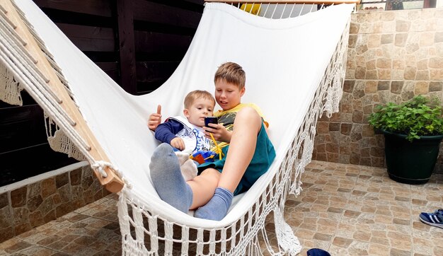 Portrait d'un mignon petit garçon allongé avec son frère aîné dans un hamac et utilisant un smartphone