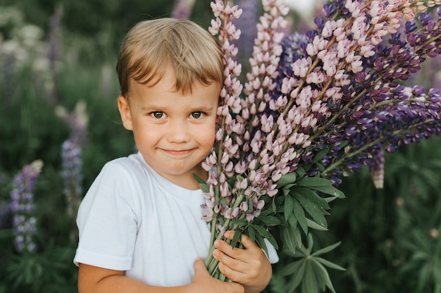 Portrait d'un mignon petit garçon heureux avec bouquet de lupins en fleurs