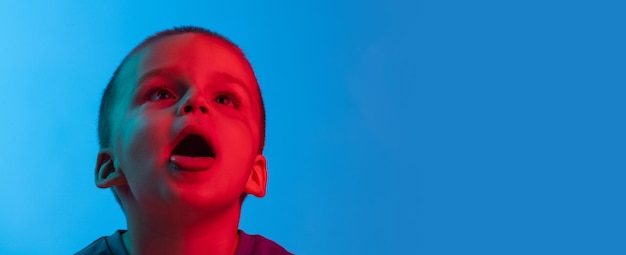 Portrait d'un mignon petit garçon posant isolé sur fond bleu à la lumière du néon Faire des grimaces Flyer