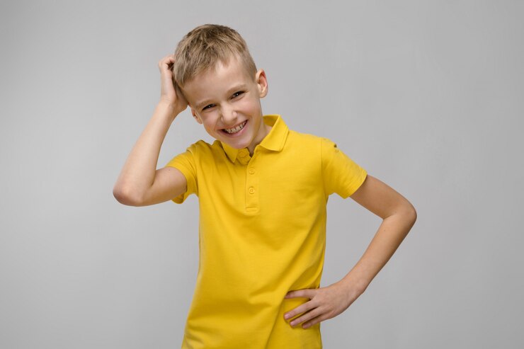 Portrait de mignon petit garçon de race blanche blonde en t-shirt jaune pensant sur gris
