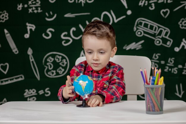 Portrait de mignon petit garçon tenant en mains petit globe sur fond de tableau noir. Prêt pour l'école. Retour à l'école.