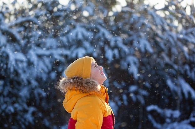 Portrait d'un mignon petit garçon en vêtements d'hiver jaune qui attrape la bouche des flocons de neige en hiver. Enfant dans une neige qui tombe.