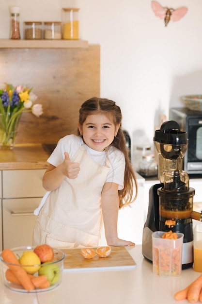 Portrait d'une mignonne fille de cinq ans en tablier préparant des fruits et légumes biologiques pour du jus frais