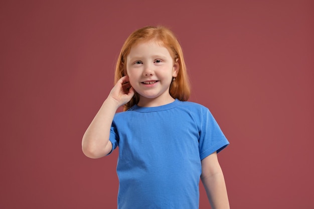 Portrait de mignonne petite fille émotionnelle rousse sur fond rouge