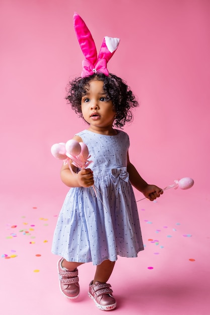 portrait d'une mignonne petite fille avec des oreilles de lapin de Pâques sur sa tête tenant des oeufs de Pâques. studio, fond rose