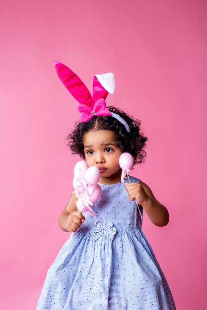 portrait d'une mignonne petite fille avec des oreilles de lapin de Pâques sur sa tête tenant des oeufs de Pâques. studio, fond rose