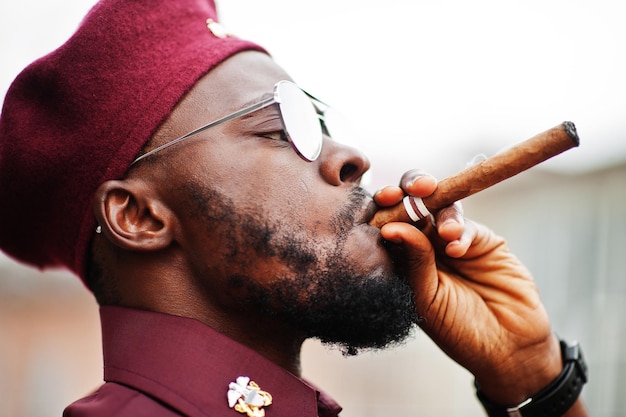 Portrait d'un militaire afro-américain en uniforme rouge, lunettes de soleil et béret. Le capitaine fume un cigare.