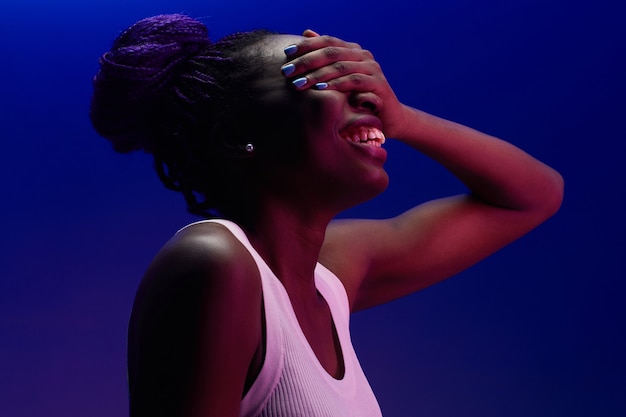 Portrait minimal d'une femme afro-américaine insouciante riant alors qu'elle est éclairée par une lumière violette en studio