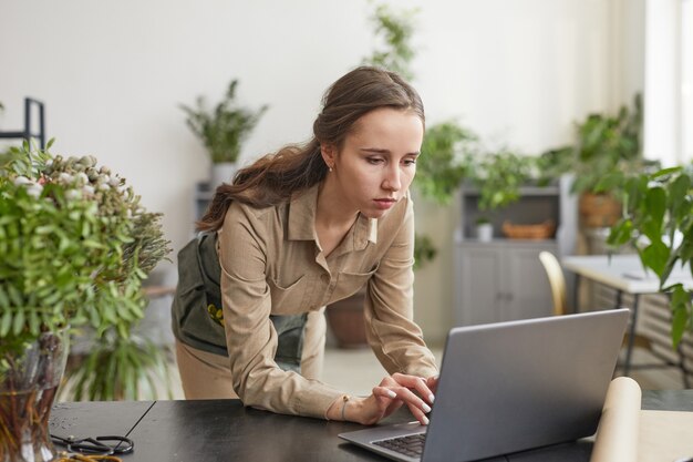 Portrait minimal d'une jeune fleuriste utilisant un ordinateur portable tout en gérant un atelier de petite entreprise, un espace de copie