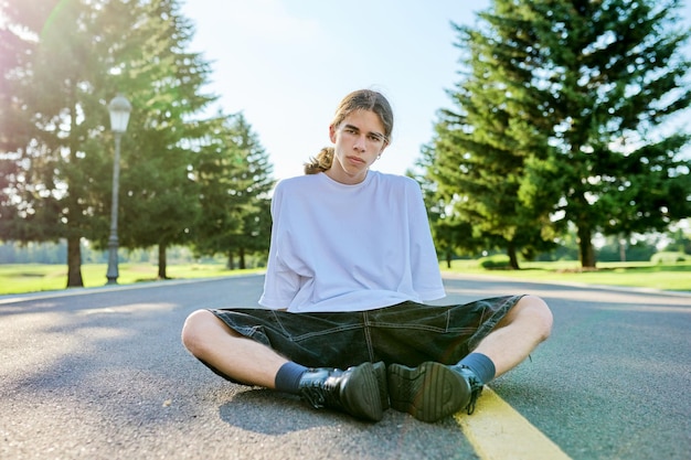 Portrait de mode d'un adolescent hipster assis sur la route