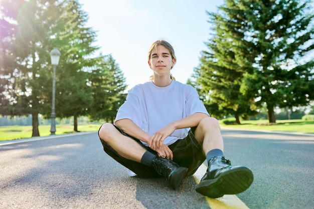 Portrait de mode d'un adolescent hipster assis sur la route