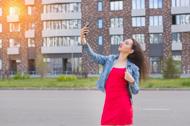 Portrait de mode d'une belle fille vêtue d'une élégante robe rouge avec une aube d'été dans la ville