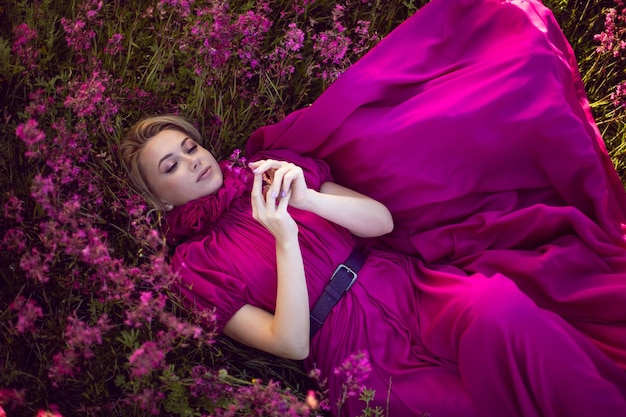 Portrait à la mode belle jeune femme allongée dans une robe rose dans un champ de fleurs sauvages en été au coucher du soleil