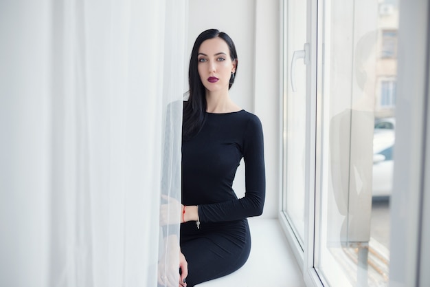 Portrait de mode. Célébrer la fête d'anniversaire. Jeune femme brune en robe noire posant sur blanc