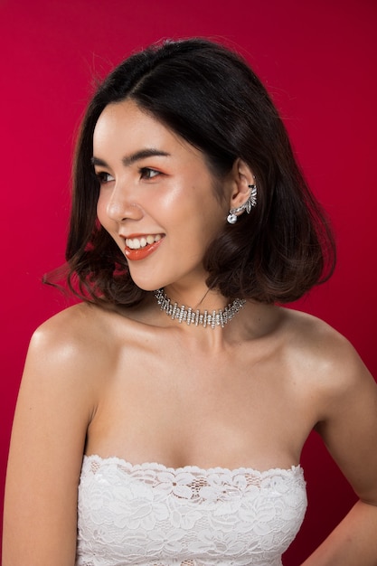 Portrait de mode d'une femme asiatique à la peau bronzée aux cheveux noirs avec des lèvres rouges de couleur super forte portant un collier de boucles d'oreilles en diamant de fourrure blanche, éclairage de studio fond rouge rougeâtre copie espace texte logo