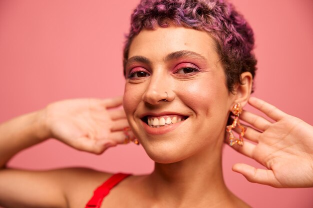 Portrait de mode d'une femme avec une coupe de cheveux courte de couleur violette et un sourire avec des dents dans un haut rouge sur fond rose bonheur