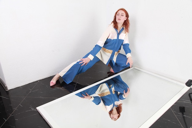 Photo portrait à la mode d'une femme élégante dans un costume à rayures blanches bleues d'été assise près d'un miroir réfléchissant