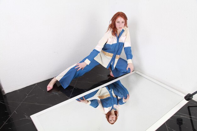 Portrait de mode d'une femme élégante en été en costume à rayures bleues et blanches assise près d'un miroir réfléchissant