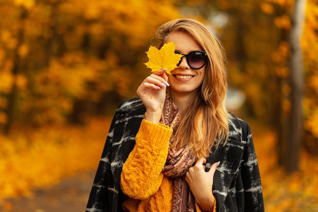 Portrait de mode fraîche d'une jeune femme avec des lèvres sexy dans des lunettes de soleil rondes élégantes et un chapeau de paille inélégant dans une belle robe rayée. Mannequin de jolie fille à l'extérieur. Vêtements d'été à la mode