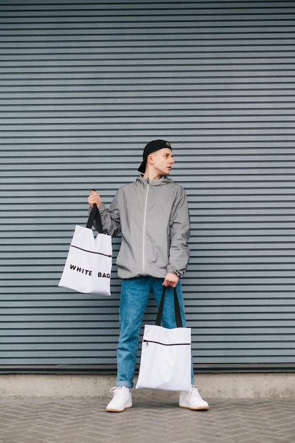 Le portrait à la mode d'un gars en vêtements décontractés se dresse sur un fond de mur gris