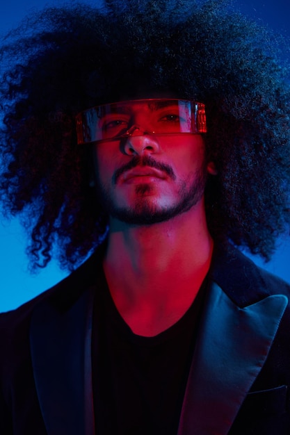 Portrait de mode d'un homme aux cheveux bouclés sur fond bleu portant des lunettes de soleil rouges concept moderne à la mode lumière multinationale