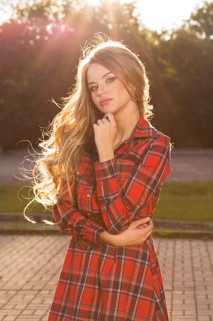 Portrait de mode d'un modèle blond élégant en robe tendance posant dans les rayons du soleil