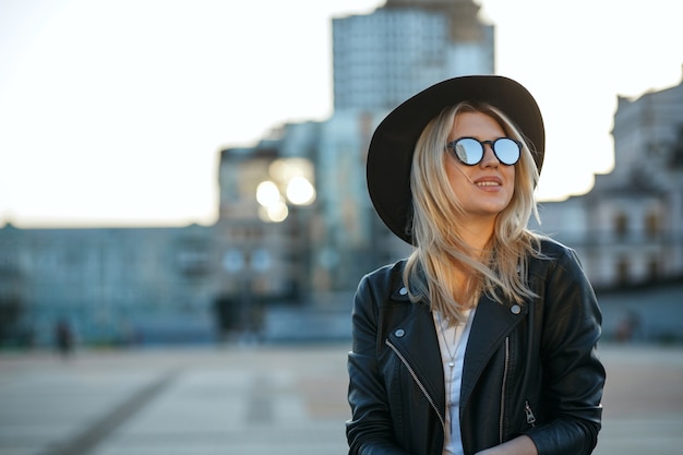 Portrait de mode en plein air d'une femme blonde joyeuse portant un chapeau et des lunettes de soleil miroir. Espace pour le texte