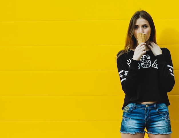 Portrait de mode en plein air de jeune fille hipster avec glace sur fond de mur jaune