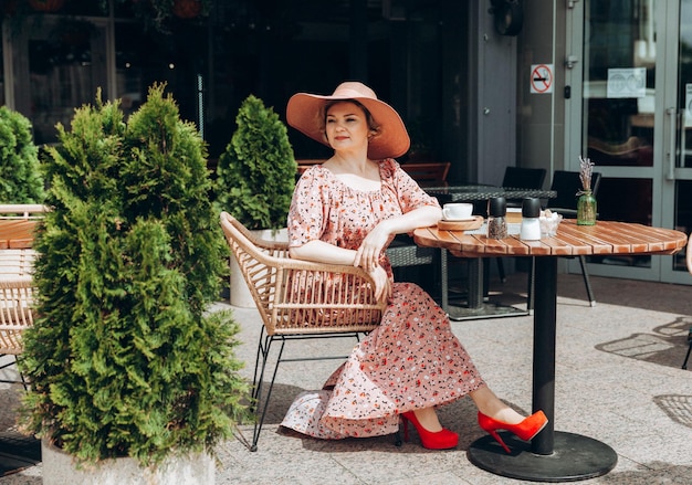 Portrait de mode en plein air d'une superbe femme assise dans un café Je bois du café et lis un vieux livre une femme en robe et un chapeau