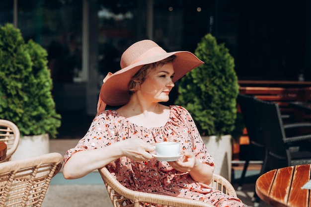 Portrait de mode en plein air d'une superbe femme assise dans un café Je bois du café et lis un vieux livre une femme en robe et un chapeau