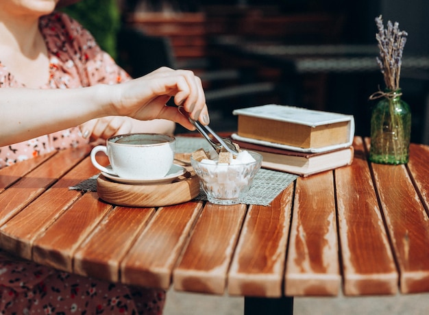 Portrait de mode en plein air d'une superbe femme assise dans un café Je bois du café et lis un vieux livre une femme en robe et un chapeau