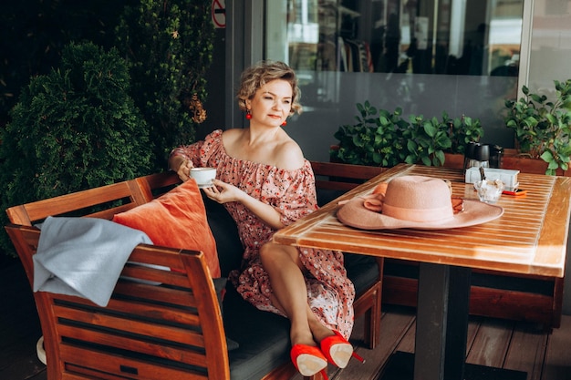 Portrait de mode en plein air d'une superbe femme assise dans un café Je bois du café et lis un vieux livre une femme en robe et un chapeau