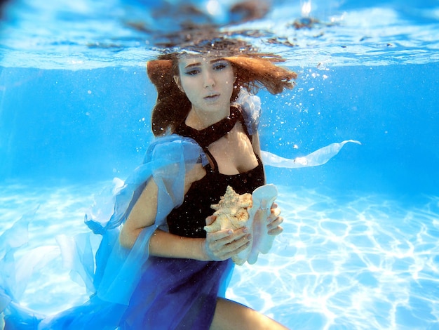 Portrait de mode sous-marine de la belle jeune femme en robe bleue